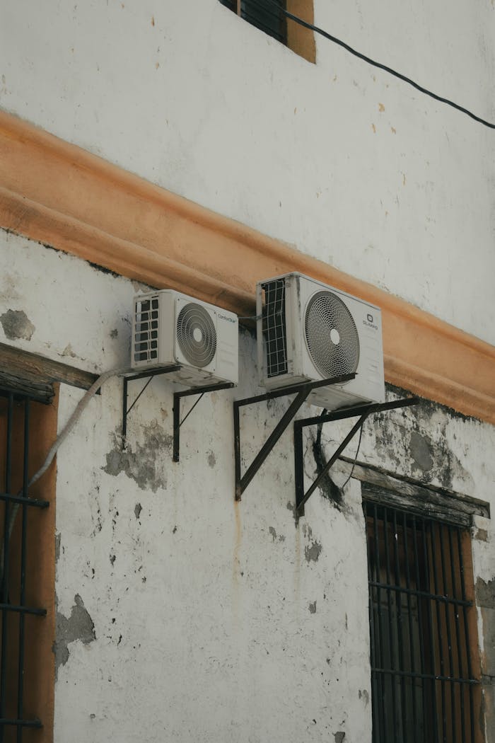 Two outdoor AC units installed on a weathered concrete wall for cooling purposes.